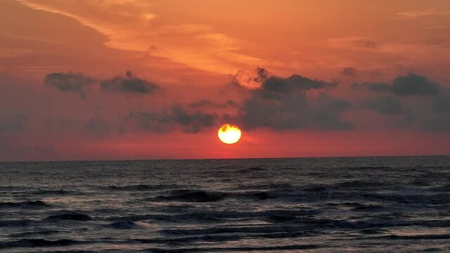 Aerial view of the sun rising over the sea, casting a warm orange glow across the sky and reflecting on the water's surface, Gilan, iran.