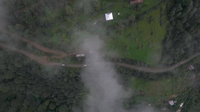 Aerial view of winding dirt road cutting through lush green forests, partially obscured by low-lying clouds, Talesh, Gilan Province, iran.