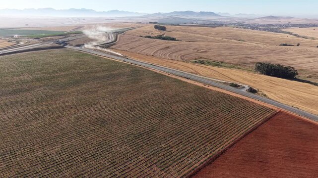 Aerial view of vibrant green and red fields meet the R45 highway under a sunny sky, creating a striking contrast in Malmesbury, Western Cape, South Africa.