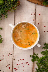 Classic chicken noodle soup with herbs served in a white bowl on rustic wooden table