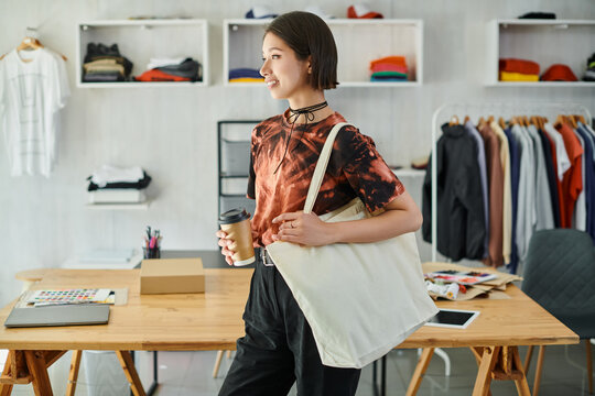 Young woman running a print studio while holding a coffee cup and a tote bag