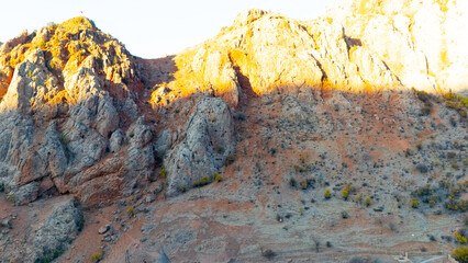 Top-down drone view of a winding asphalt road cutting through bright red earth and dry terrain. Strong geometric shapes and vibrant colors create a striking abstract landscap