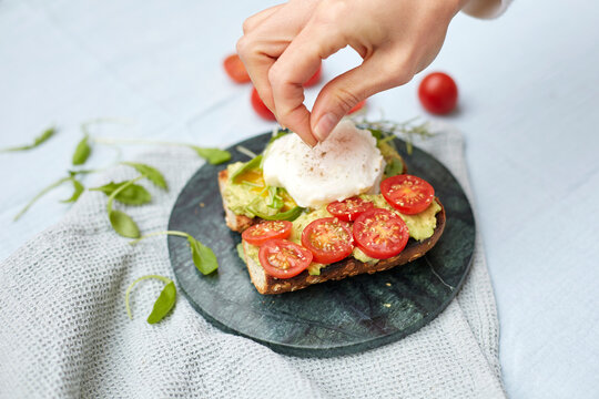 Hand preparing poached egg on avocado toast