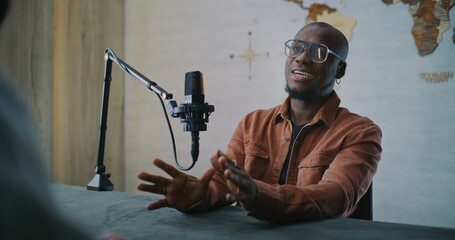 Confident Podcast Guest Engaged in Thoughtful Studio Discussion. African American Man Participates in Mindful Dialogue, Smiling as Responds to Host Across Table in Modern Podcast Studio. Portrait.