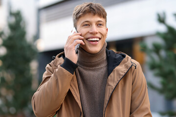 Portrait of smiling man in jacket talking by smartphone on city street