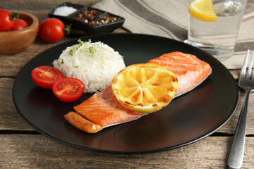 Piece of tasty grilled salmon, lemon, tomato, rice and microgreens on wooden table, closeup