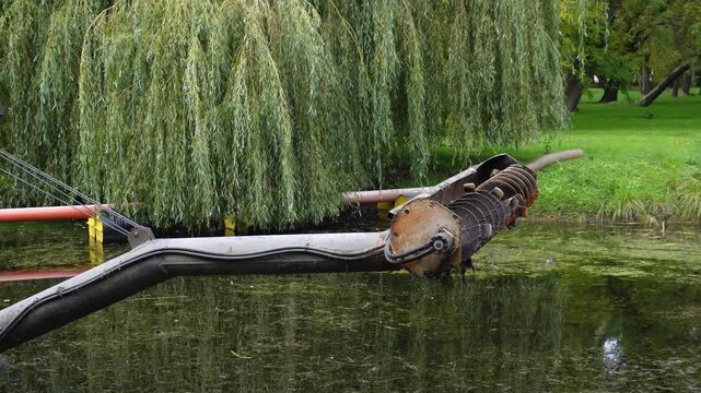 Unique mechanical fish sculpture in a serene park setting surrounded by water and green trees