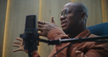 Close Up of Adult Male Expert Wearing Glasses and Earring, Actively Gesturing While Talking Into Professional Studio Microphone. Concept of Confident Digital Broadcasting and Thought Leadership.