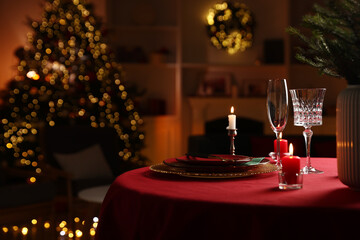 Christmas table setting with plates, glasses and burning candles in festive decorated room. Bokeh effect