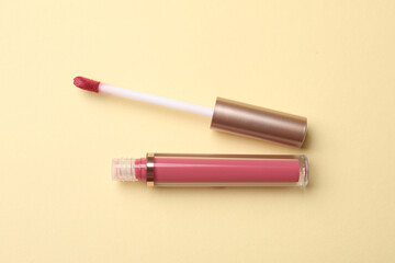 Beautiful lip gloss with applicator on beige background, top view