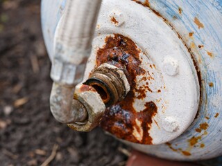 A close-up view of a rusted and leaking metal pipe connection on an old outdoor water tank, highlighting corrosion and material decay.