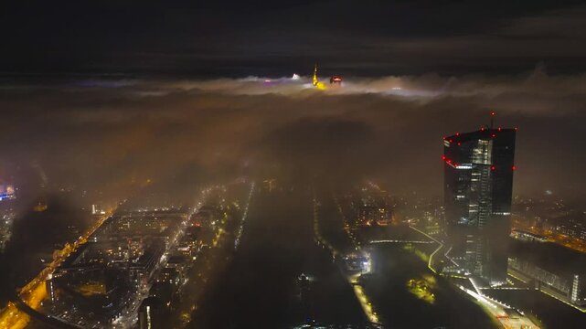 Aerial view of skyscrapers piercing through a thick blanket of fog, illuminated by city lights creating an ethereal glow, Frankfurt am Main, Hessen, Germany.