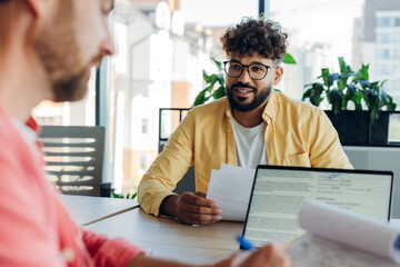 Confident men working together in modern office talking sitting on workplace