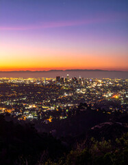 Obraz premium Panoramic view of Los Angeles at dusk. Cityscape with glowing lights, a vibrant gradient sky, and distant mountains at sunset.