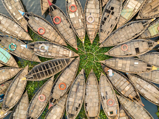 Aerial view of wooden boats arranged in a radial pattern around a central hub of green vegetation, creating a striking contrast of textures and tones, Dhaka, Dhaka Division, Bangladesh.