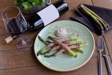 Grilled asparagus with bacon on a plate on a table with a bottle of wine