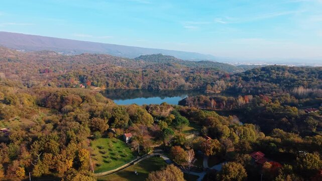 Aerial view of the tranquil Lake Pistono mirroring the sky, nestled amidst a vibrant forest in autumn colors, Montalto Dora, Piedmont, italy.