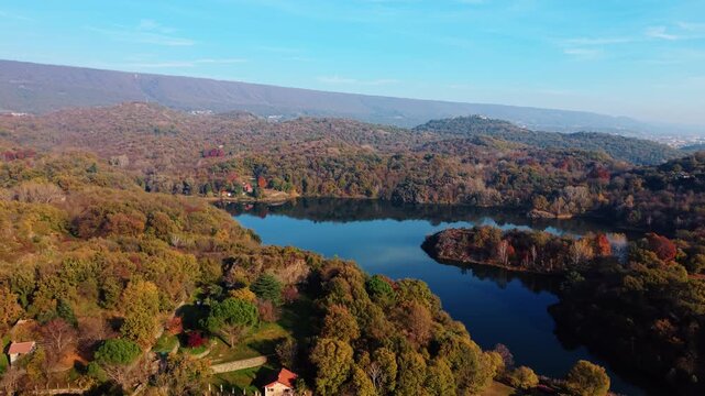 Aerial view of the calm, dark blue waters of Lake Pistono surrounded by the colorful autumn foliage of Montalto Dora, Piedmont, Italy.