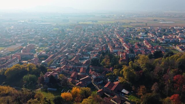 Aerial view of the cityscape with red-tiled roofs contrasting with the green foliage and distant fields of Montalto Dora, Piedmont, Italy.