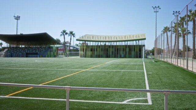 Football pitch with soft defocused bokeh background, turf foreground and distant stands blurred outdoor; background backplate copyspace calm.