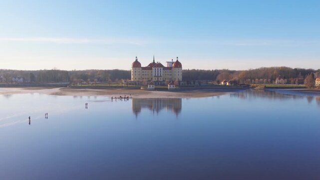 Moritzburg Castle stands before a wide frozen lake whose icy surface reflects the baroque scenery in crisp winter light.