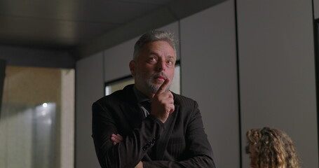 Close up of mature businessman with hand on chin and focused expression while considering decision during corporate meeting in modern office