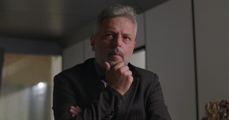 Obraz premium Close up of mature businessman with hand on chin and focused expression while considering decision during corporate meeting in modern office