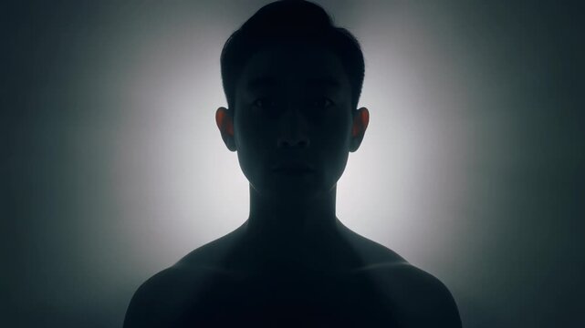 Silhouette of Young Man's Head and Shoulders Against Bright Light Source stock dark
