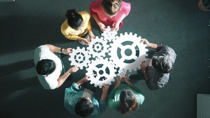 Top down aerial view of business team working together to gather cog together. Aerial view of professional diverse group holding cog and complete white gear. Represented unity, teamwork. Symposium. © InfiniteFlow