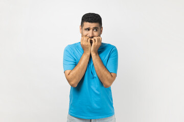 Man bites finger nails with nervous expression, stares away with eyes full of fear.