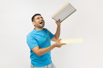 Sad upset crying man in blue T- shirt standing holding opened present box, looks inside with despair