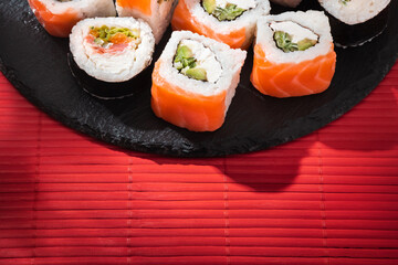 Philadelphia sushi roll salmon on round slate board and red bamboo mat in soft sunlight.