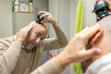 Man shaving head with electric shaver in bathroom
