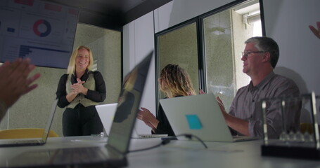 Businesswoman smiling and receiving applause from colleagues after delivering successful...