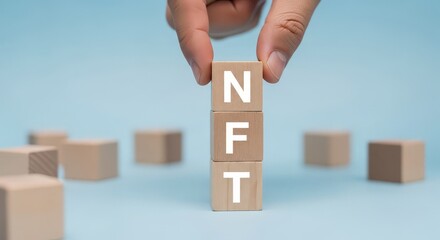 Hand placing n block on top of f and t blocks to spell nft against a light blue background