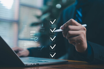 Businessman marking digital checkboxes on a laptop, showing task management, checklist review,...