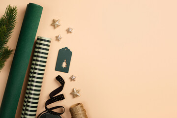 Christmas wrapping paper rolls, green gift tag, and gold stars on beige background. Copy space for holiday text or design.