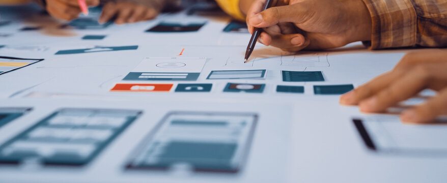A dynamic team collaborates on user interface design using sketches and wireframes on a shared workspace, highlighting teamwork and creativity in digital project development. SACTR