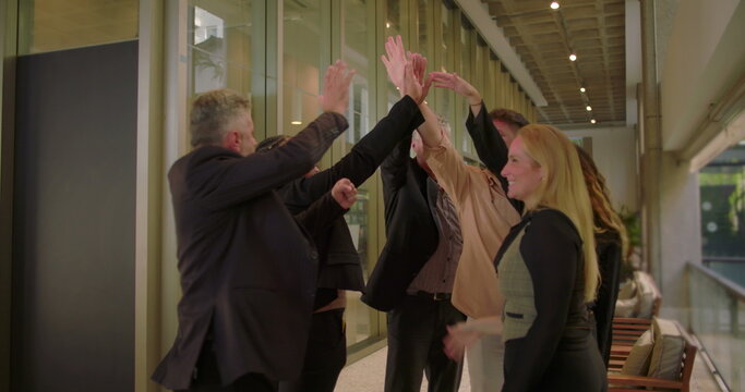Cheerful business group giving high five indoors, coworkers acknowledging team success and unity in collaborative professional atmosphere