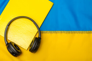 Fluent in Ukrainian. Learn Ukrainian. Audio Book, Listening Music in Ukrainian Language. Headphones and Notebook  on Ukraine Flag Background. 