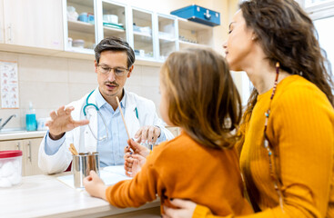 Obraz premium Male pediatrician consulting with a woman and her young child during a medical checkup in clinic.