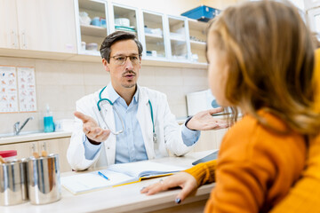 Male pediatrician consulting with a woman and her young child during a medical checkup in clinic.