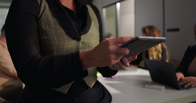 Close-up of businesswoman using tablet during office meeting, collaborative workspace with team members working in background, highlighting technology and leadership focus