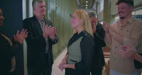 Cheerful business team clapping for female colleague in modern office hallway, diverse coworkers expressing recognition and appreciation for success