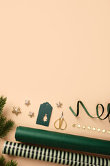 Christmas wrapping paper rolls, green gift tag, and gold stars on beige background. Copy space for holiday text or design.