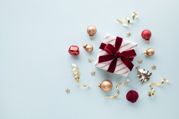 Obraz premium Gift box golden wrapped with red velvet ribbon on light blue backdrop decorations festive bauble and stars for Christmas and New Year greeting card