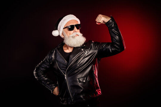 Cool santa rocker in leather jacket flexing bicep wearing santa hat and sunglass for christmas themed fashion promo