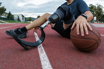 A man with a prosthetic leg is actively playing basketball on an outdoor court with friends during the late afternoon.