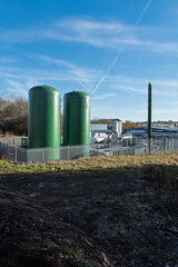 Two large green metal silos fenced in at an industrial factory site; shot on a clear crisp autumn day.