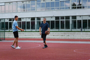 Obraz premium A man with a prosthetic leg enjoys playing basketball with a friend outside on a court during the evening.